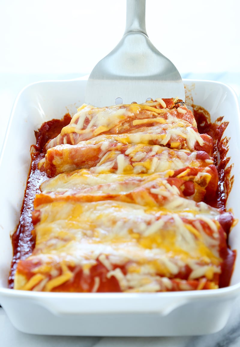 Metal spatula serving gluten free enchiladas from white casserole dish