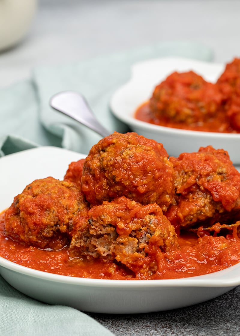 Gluten free meatballs in tomato sauce in white dish with one meatball broken in half