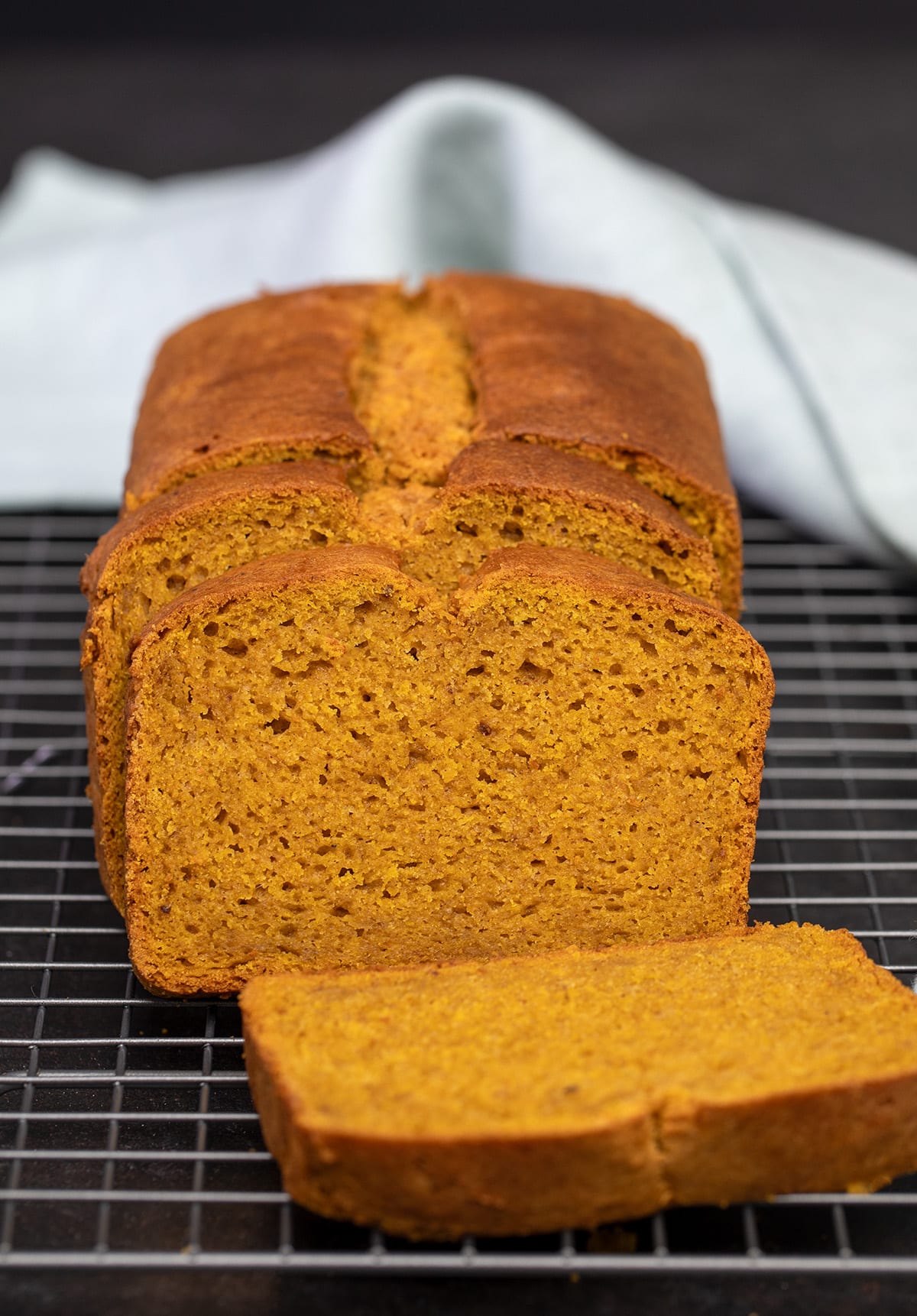 Gluten free pumpkin bread partly sliced on wire rack with light blue cloth