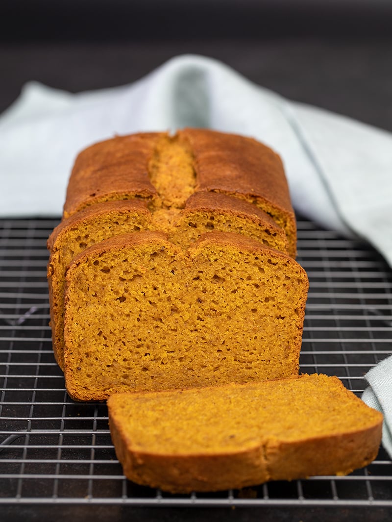 Gluten free pumpkin bread partly sliced on wire rack with light blue cloth