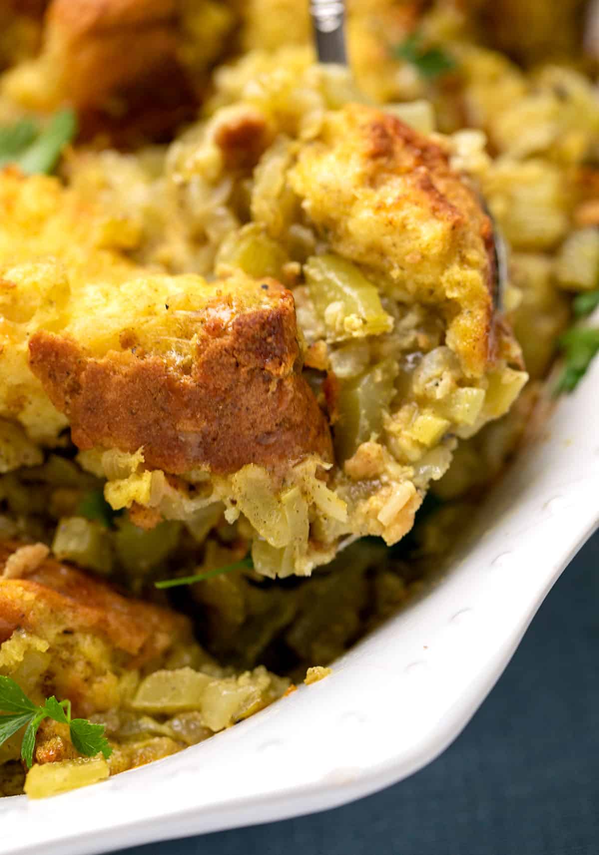 spoonful of brown bread chunks in light green and yellow cooked vegetables in white casserole dish