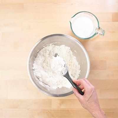 Hand holding black mixing spoon with grated butter mixed with dry ingredients