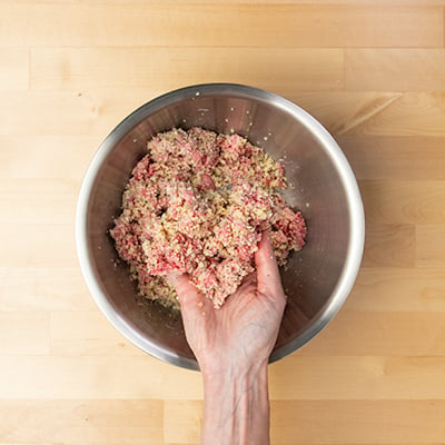 Hand holding breadcrumb mixture added to beef and cheese mixture