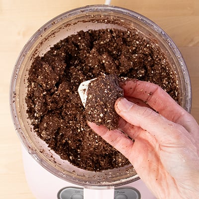 Hand holding processed dough for protein bars above food processor