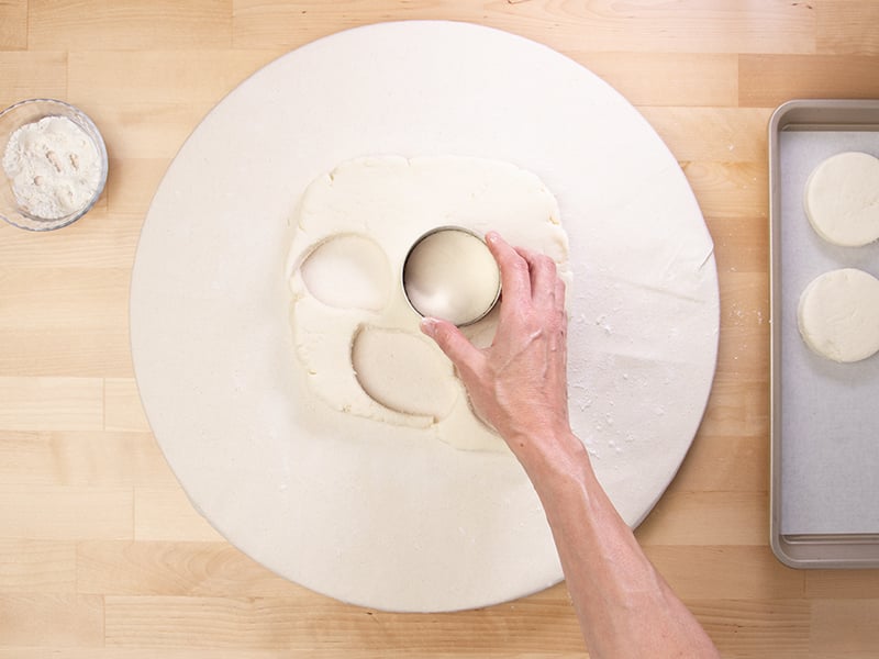 Hand holding round metal biscuit cutter on top of dough