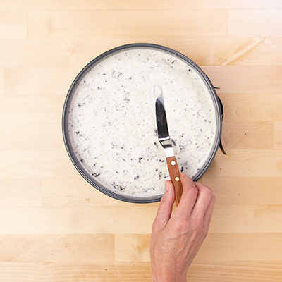 Hand holding small offset spatula smoothing top of no bake Oreo cheesecake in springform pan