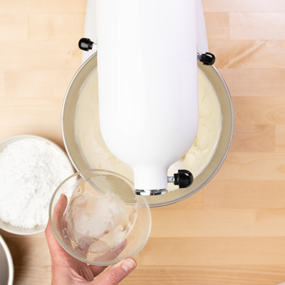 Hand pouring melted gelatin from glass bowl into stand mixer