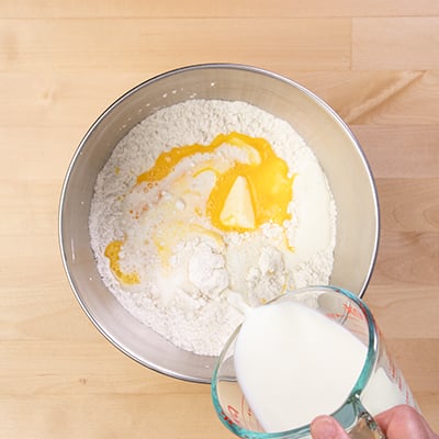 Hand pouring milk from measuring cup into metal mixing bowl