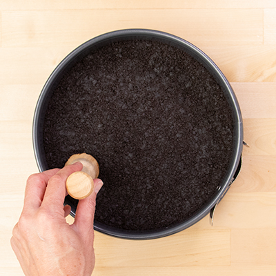 Hand pressing down chocolate cookie crumb crust in springform pan