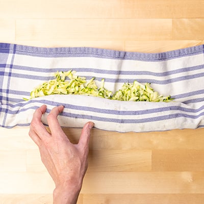 Hand rolling tea towel over shredded zucchini