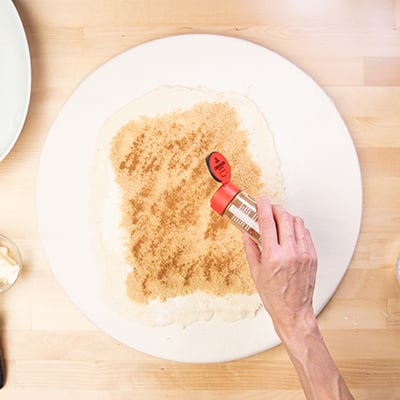 Hand sprinkling ground cinnamon on brown sugar on raw dough