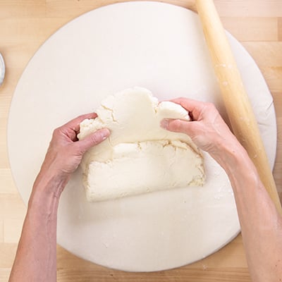 Hands folding rectangle of raw dough in thirds on white cloth