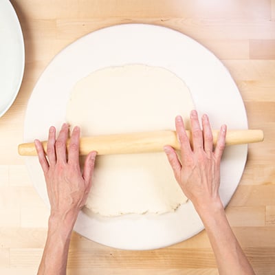 Hands on rolling pin rolling out cinnamon roll dough into rectangular shape