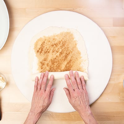 Hands rolling cinnamon roll dough into coil