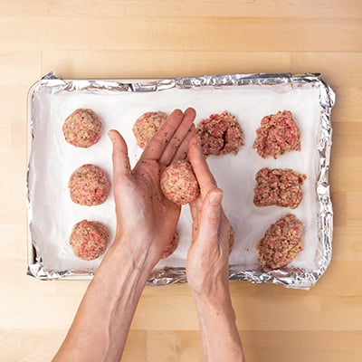 Hands rolling raw meatball into round shape