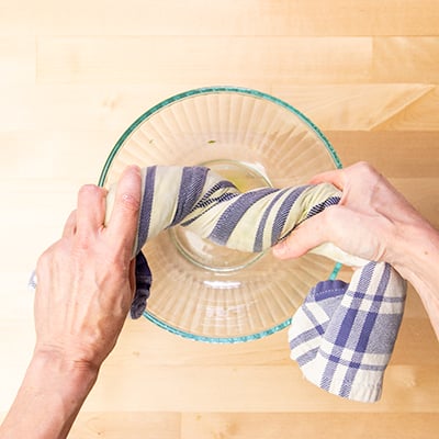 Hands twisting blue and white towel to wring out moisture into glass bowl