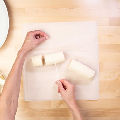 Hands using white dental floss to cut cinnamon roll dough coil