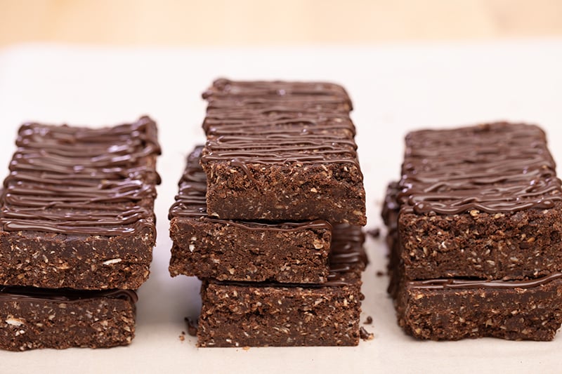 Stacks of 2 and 3 rectangular brown protein bars with chocolate drizzle