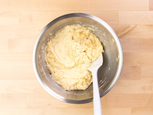 Light yellow raw banana bread batter in metal mixing bowl with white spatula