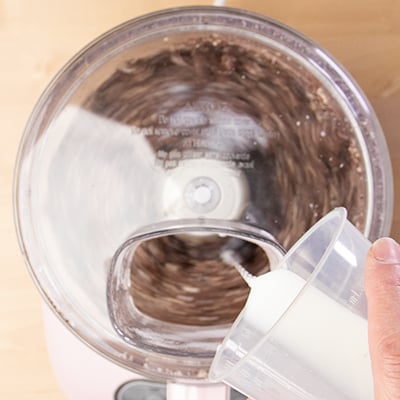 Measuring cup pouring milk into food processor chute