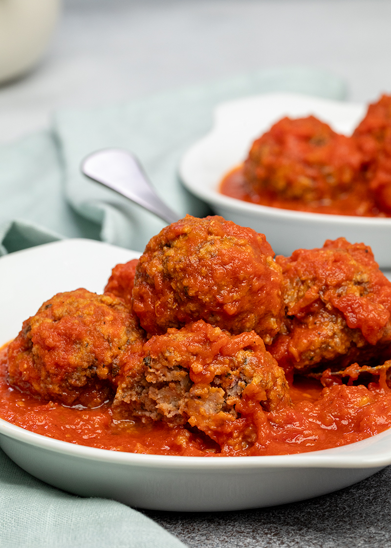 Meatballs in tomato sauce in white dish with one meatball broken in half