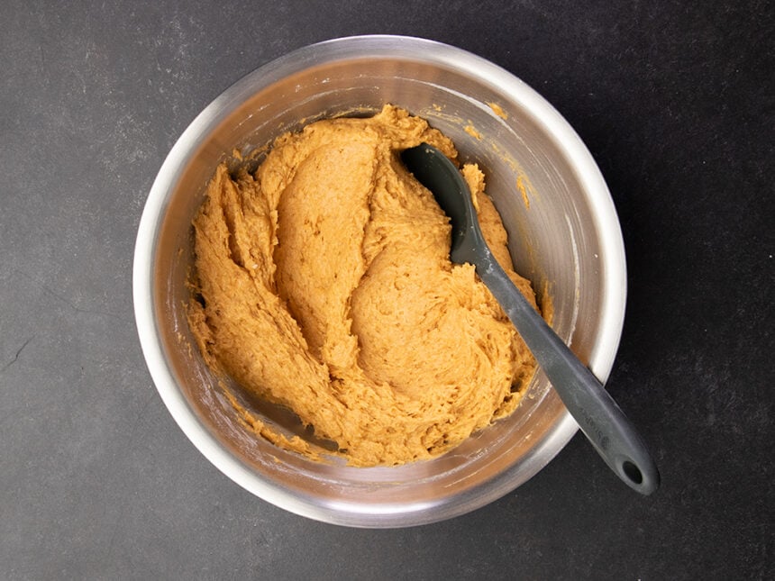 Metal mixing bowl with thick orange gluten free pumpkin butter raw batter