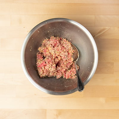 Mixing bowl with meat and breadcrumb mixture for gluten free meatballs in metal mixing bowl with metal mixing spoon