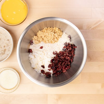 dried cranberries, oats, coconut flakes, and brown sugar in metal mixing bowl