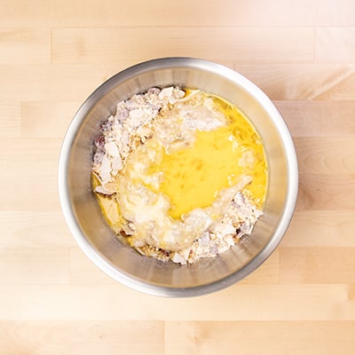 beaten eggs and mashed bananas on top of dry ingredients in mixing bowl