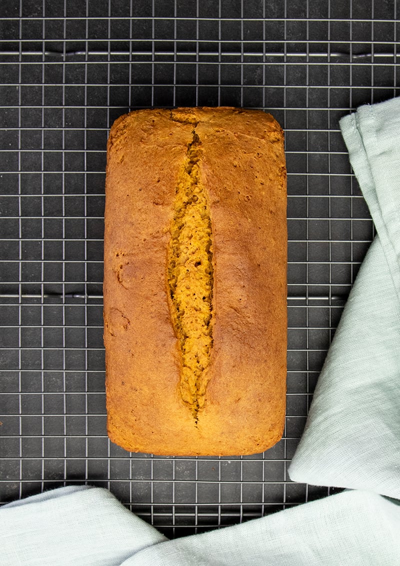 Overhead image of whole loaf of gluten free pumpkin bread on wire rack with light blue cloth