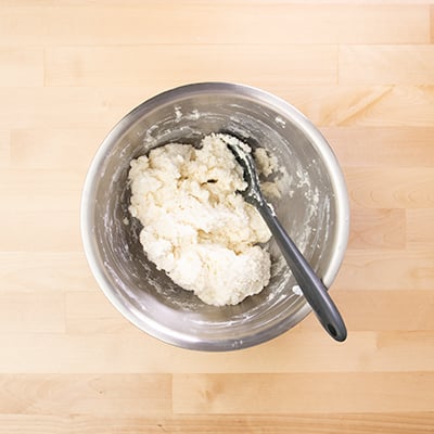 Raw biscuit dough in round metal bowl with black mixing spoon