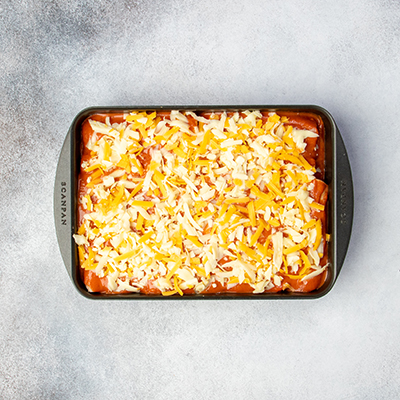 Shredded yellow and white cheese on top of red sauce in casserole dish