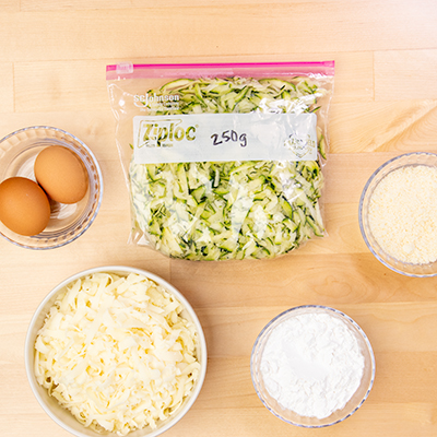 Shredded zucchini in bag stating 250 grams, bowl of eggs, bowl of shredded cheese, bowl of tapioca starch for zucchini pizza