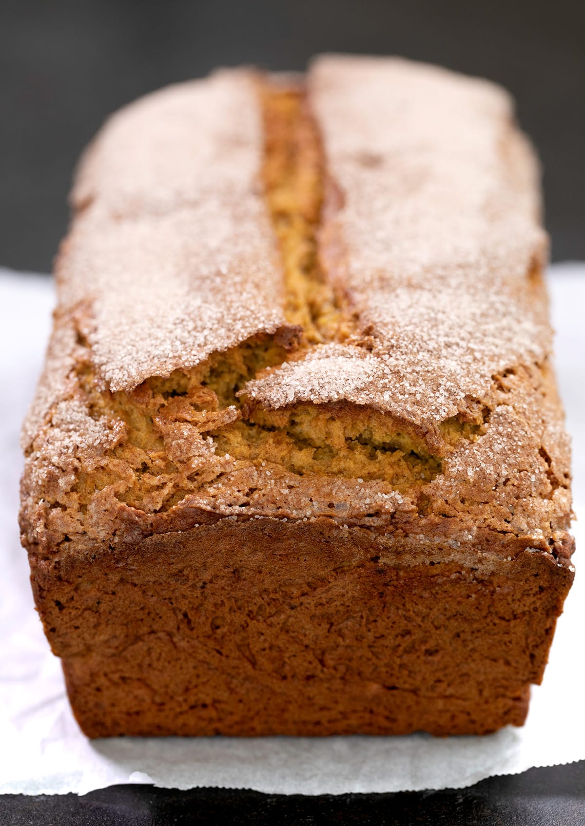 Whole baked gluten free pumpkin bread with cinnamon sugar on top sitting on white paper