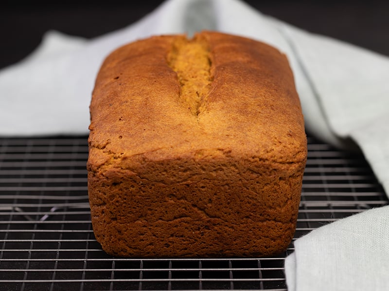 Whole loaf of pumpkin bread from side on wire rack with light blue cloth