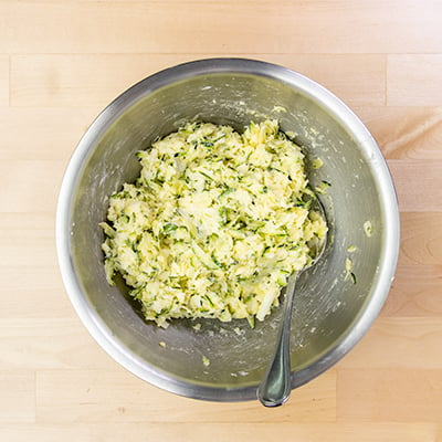 Yellow and green mixture of dough for zucchini pizza in round metal mixing bowl with mixing spoon