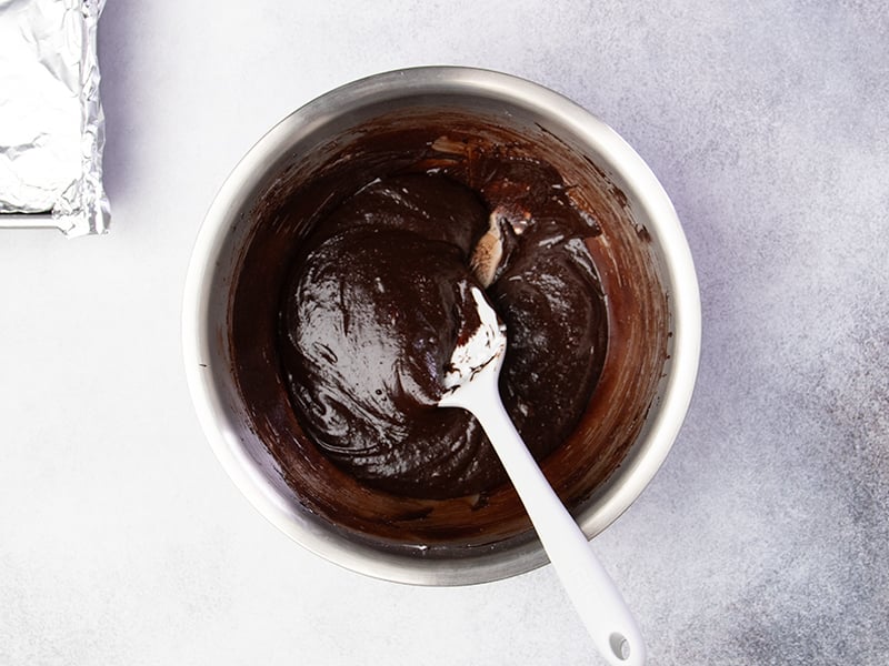 dark brown gluten free brownie batter in metal mixing bowl with white spatula