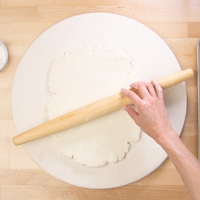 hand with rolling pin rolling out dough into rectangle on white cloth