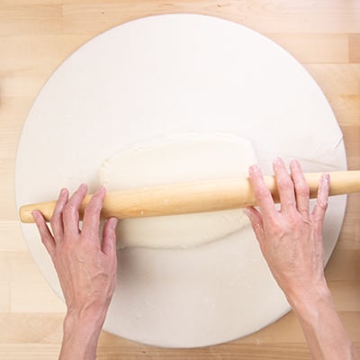 hands on rolling pin rolling dough on white cloth