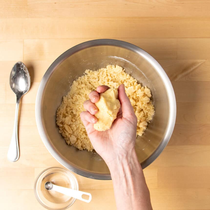 hand squeezing together light brown cracker dough over mixing bowl