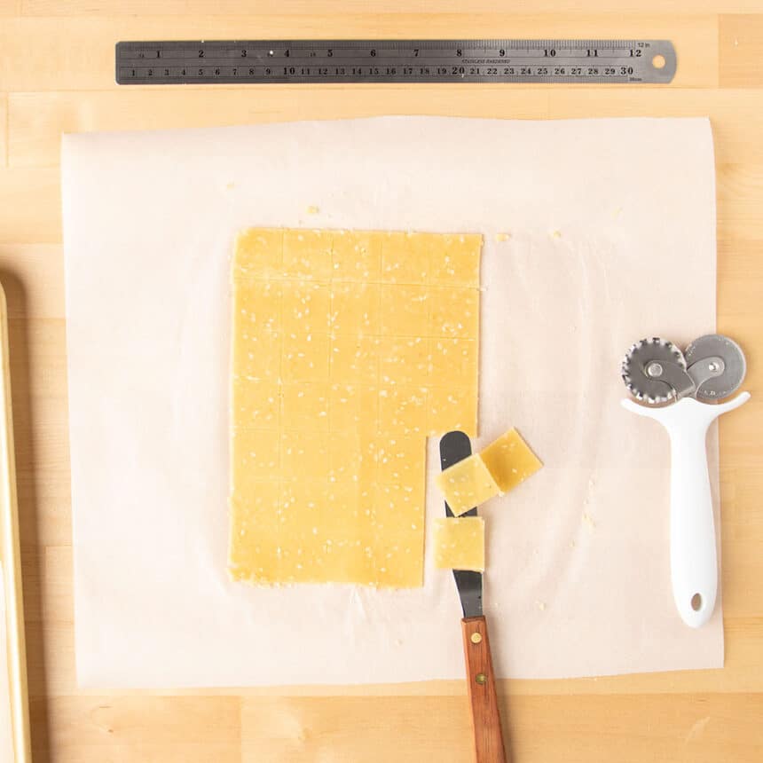 raw almond flour cracker dough cut into 1-inch squares with a few raw squares on small offset spatula