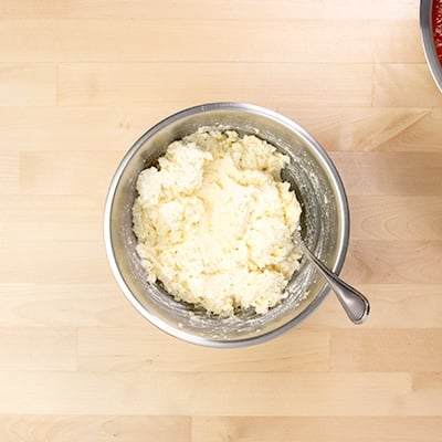 White ricotta cheese mixture in metal round mixing bowl with large metal spoon