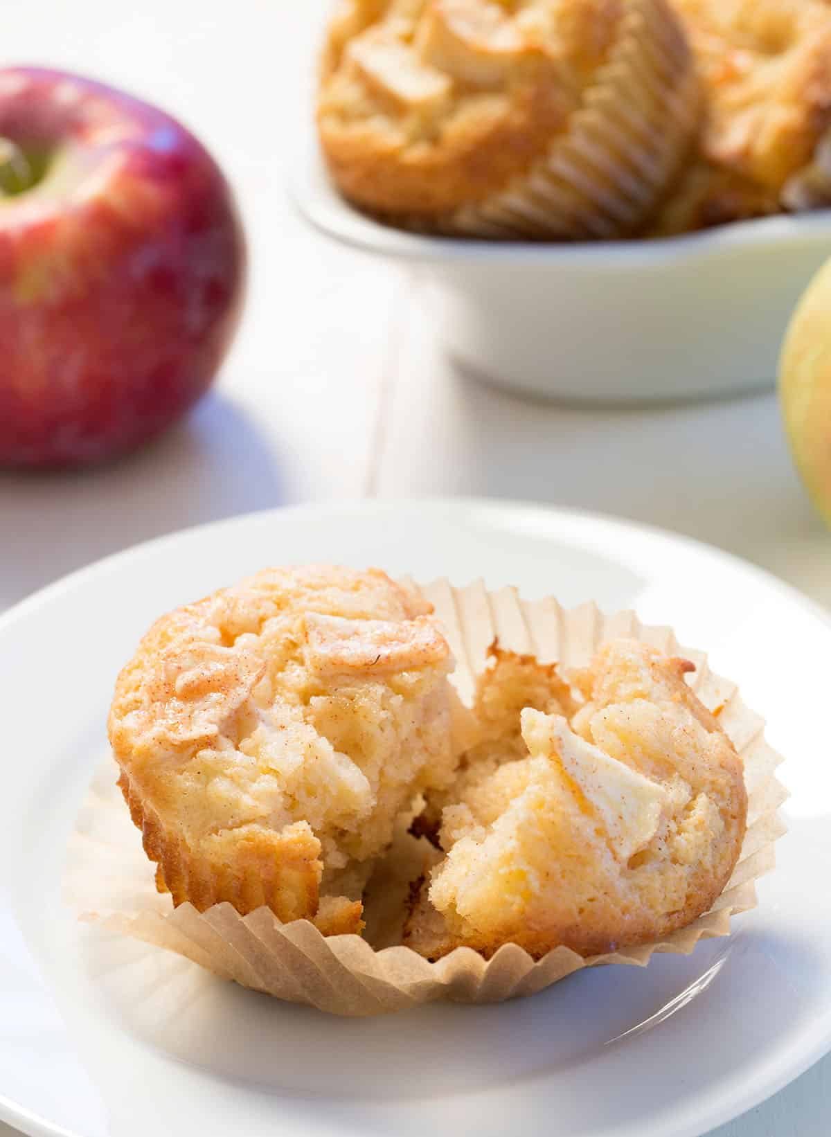 apple muffin broken in half in brown paper liner on small white plate