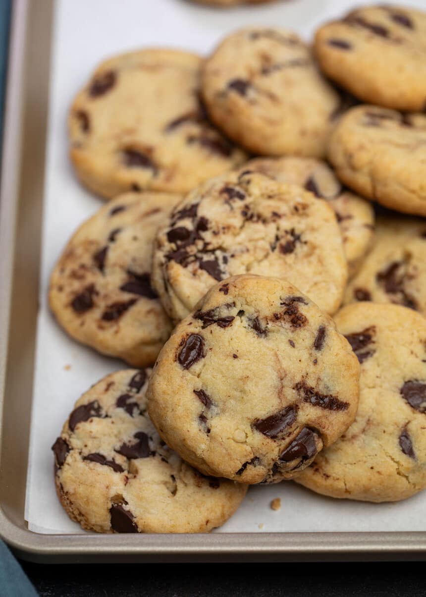 About 1 dozen thick light brown cookies with chocolate chips on white paper on baking sheet