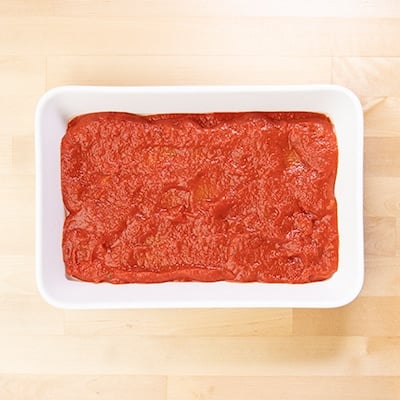 Tomato sauce on top of lasagna noodles in white casserole dish