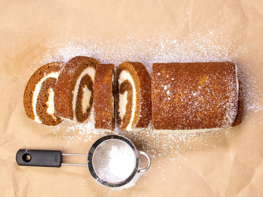 Overhead image of orange cake roll with 4 cut slices with powdered sugar in sifter