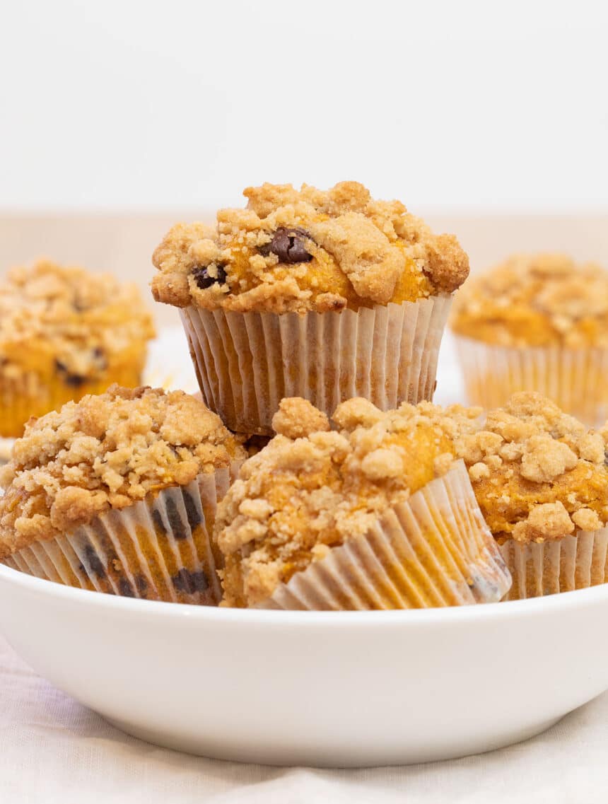 gluten free pumpkin muffins with chocolate chips and crumble topping in pile in white bowl with one on top