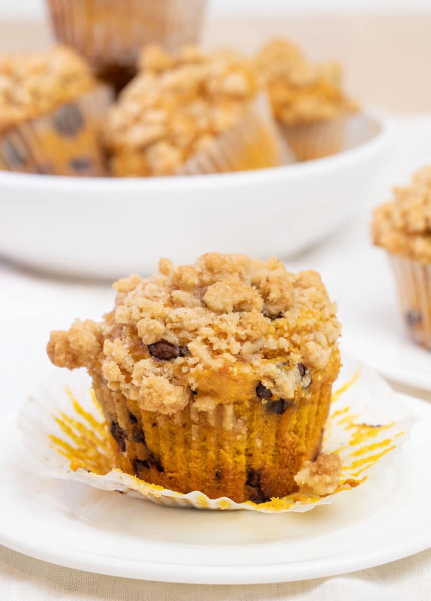 light orange muffin with light brown crumble topping with muffin liner peeled back on small white plate