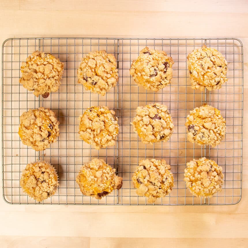 12 baked light orange pumpkin muffins with crumble topping on wire rack cooling