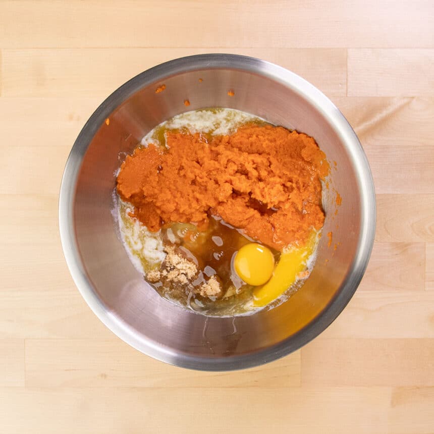 large round metal mixing bowl with orange pumpkin, yellow eggs, melted butter and sugar